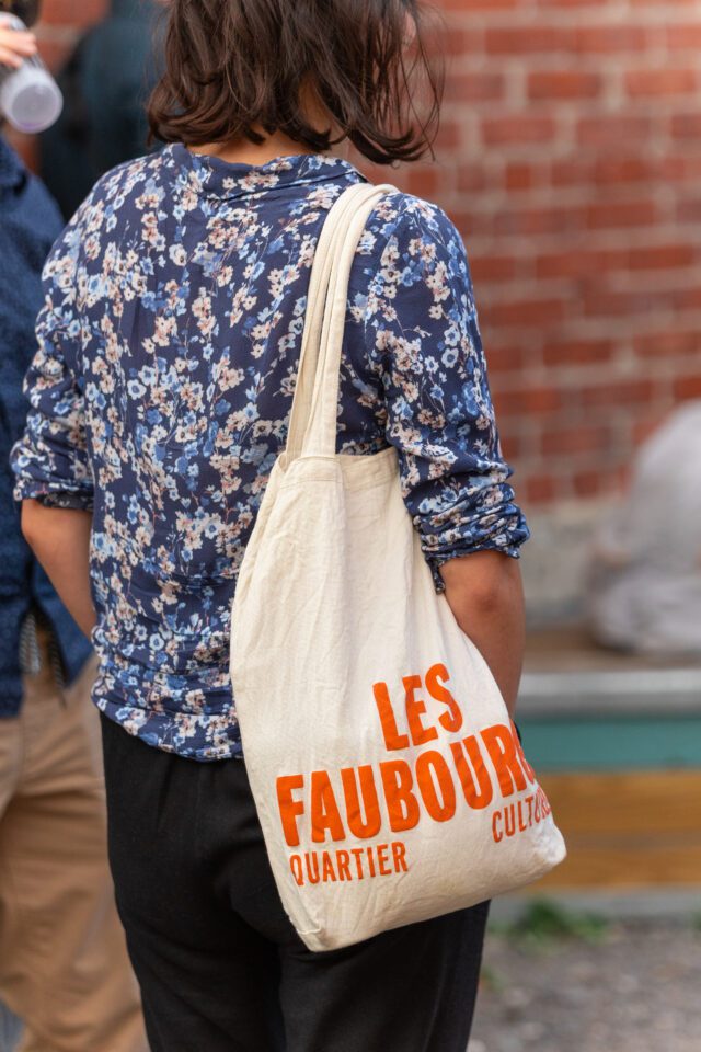 Une personne porte sur l'épaule le sac en tissu signé Les Faubourgs.